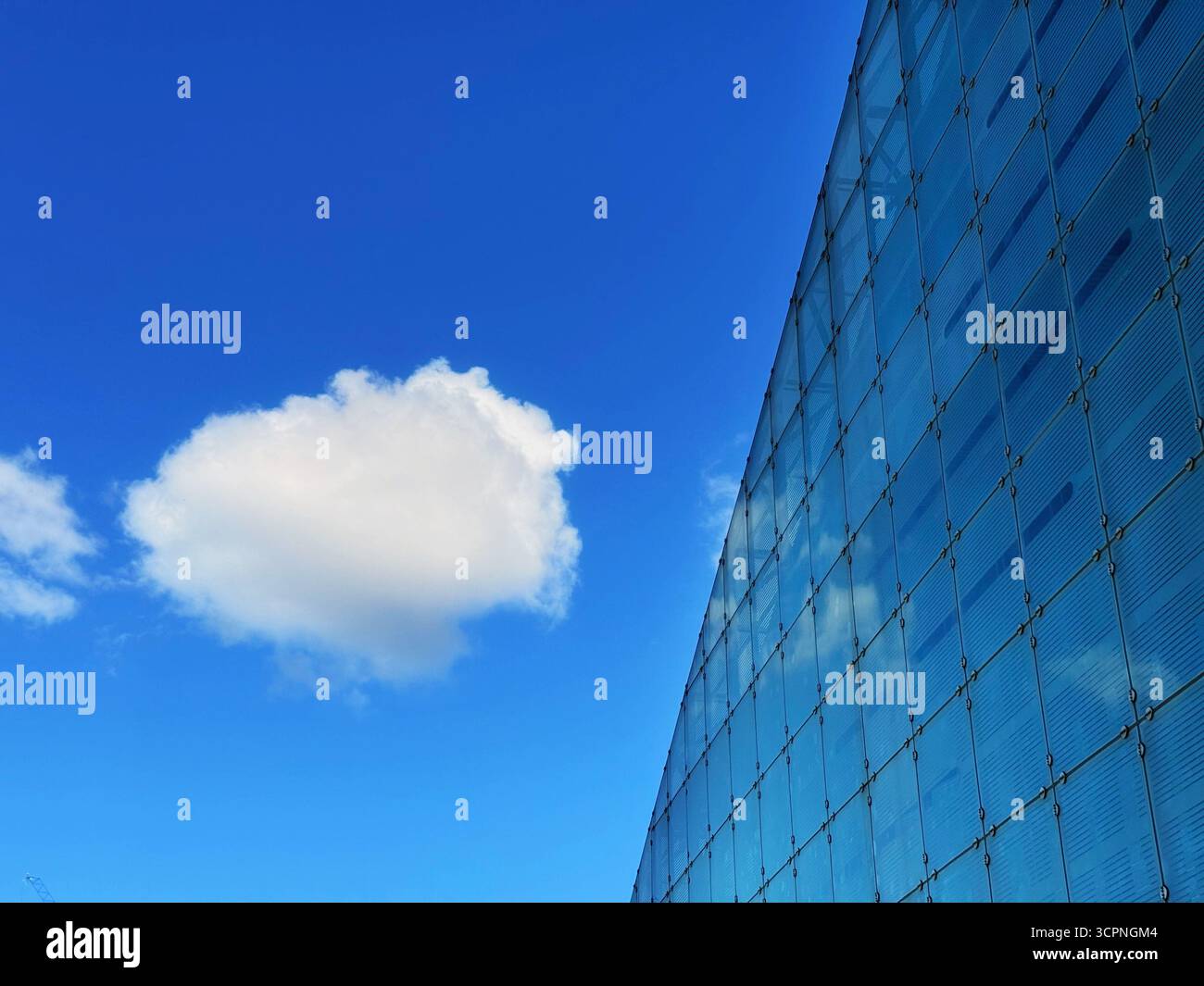 Glass side of National Football Museum (formerly Urbis building) in Manchester City centre contrasted against a fluffy white cloud and vivid blue sky. - Smartphone Captured Stock Image