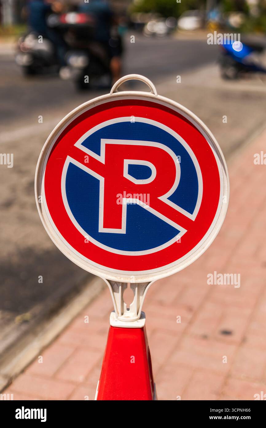A round no parking sign stands on the sidewalk in a bustling city. The ...