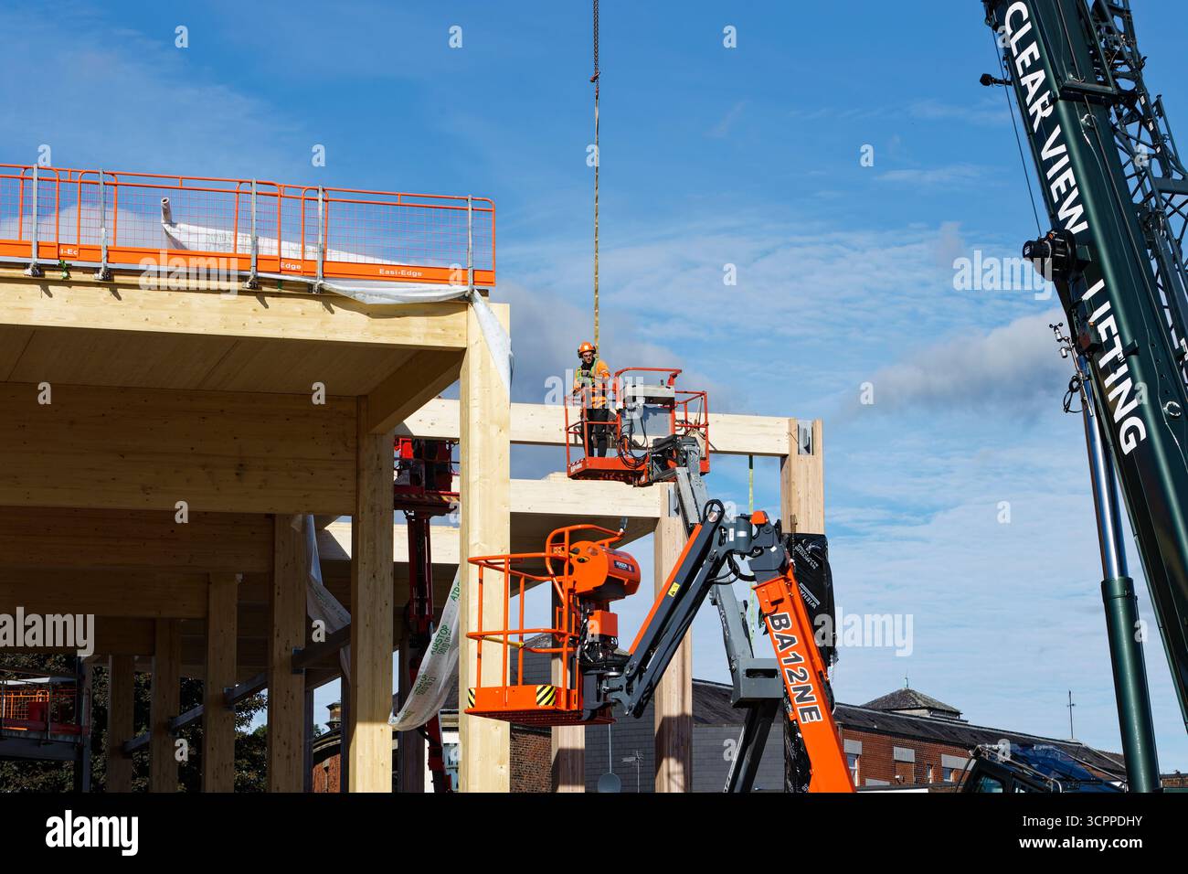 Workman Manchester Laminated timber beam suspended from crane guided onto Glulam frame by ...
