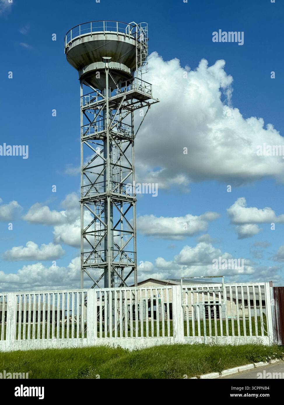 Rustic old water tower enclosed by a fence, showing vintage industrial architecture and rural infrastructure under clear skies - Smartphone Captured Stock Image