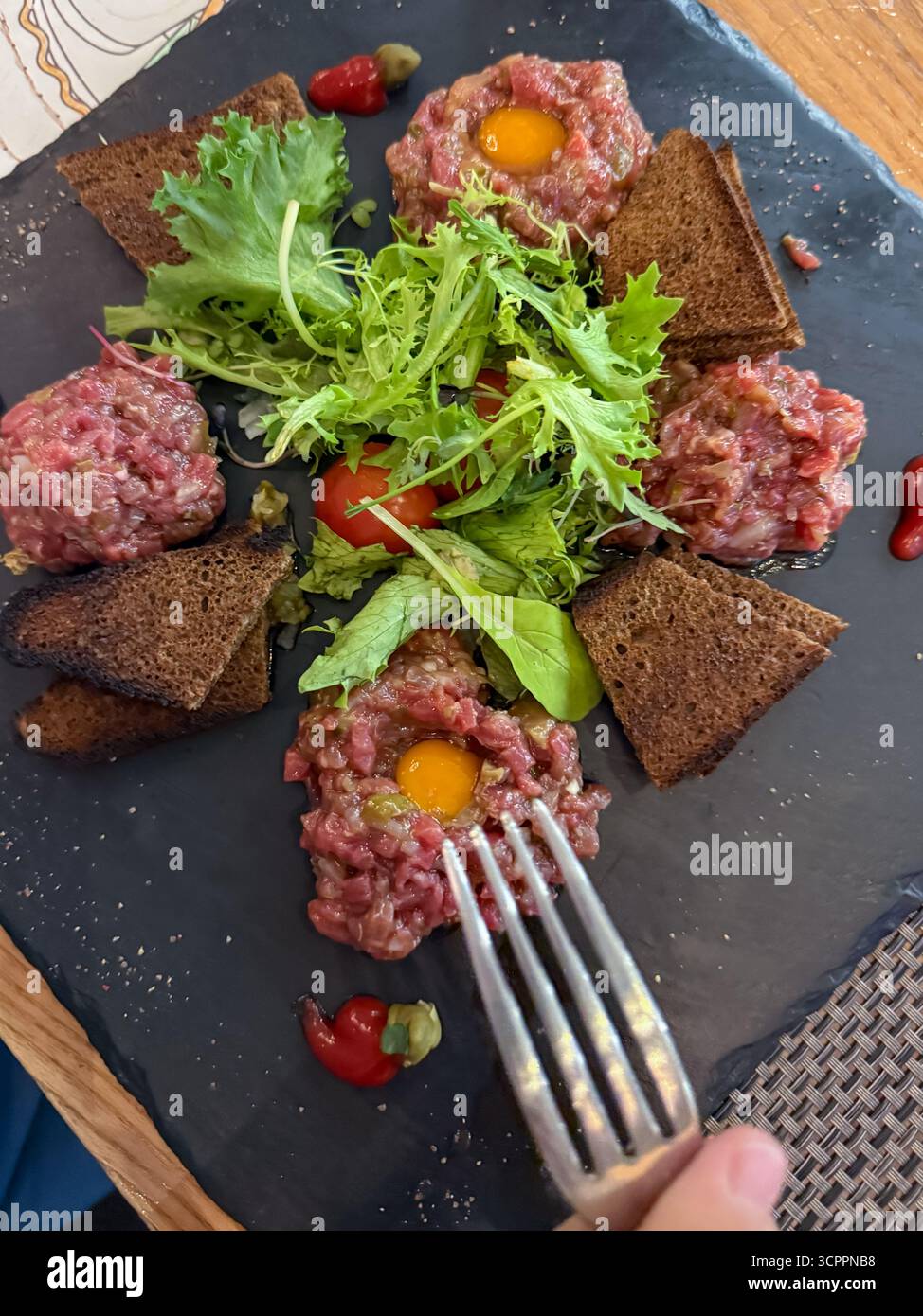Raw beef tartare plated with a raw egg, cherry tomatoes, fresh green salad, and crispy croutons, highlighting gourmet cuisine and elegant presentation - Smartphone Captured Stock Image