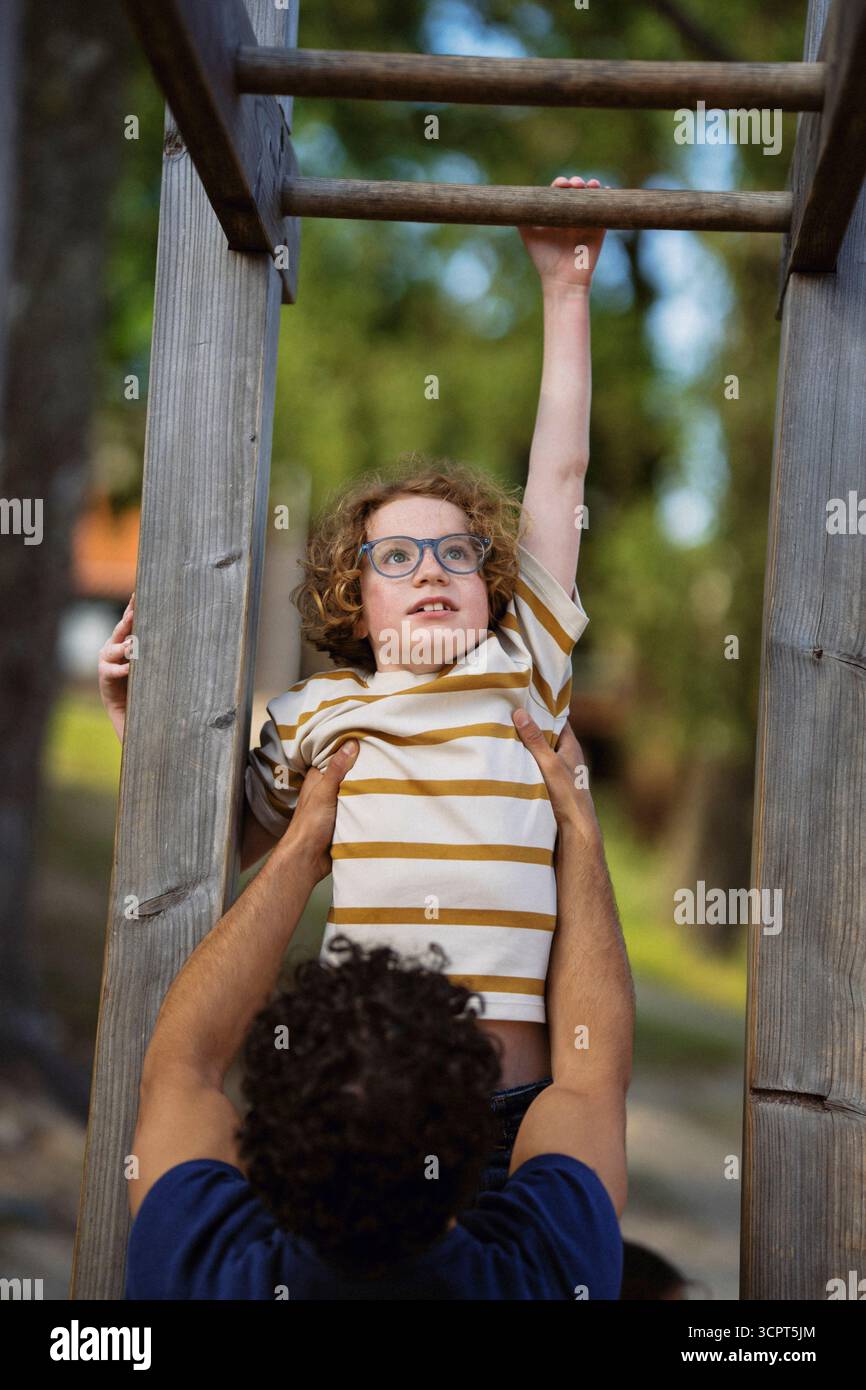 Male guide helping boy in hanging on monkey bars at summer camp Stock Photo