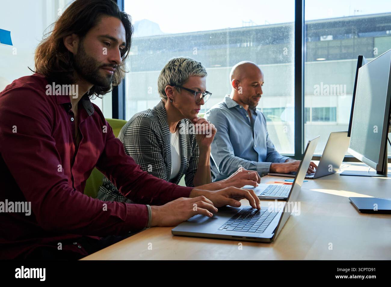 Three multiracial business colleagues sitting in the office working using laptops. Stock Photo