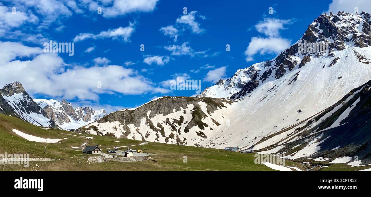 Mountain Landscape with Snow-Capped Peaks, Green Meadows and Small Alpine Huts under Clear Sky - Smartphone Captured Stock Image