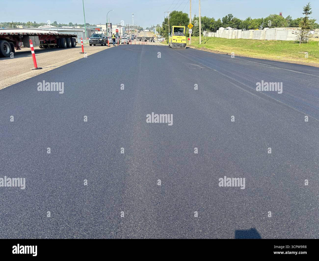 Freshly paved residential street, showing smooth new asphalt surface, and roadside trees in a suburban neighbourhood. - Smartphone Captured Stock Image
