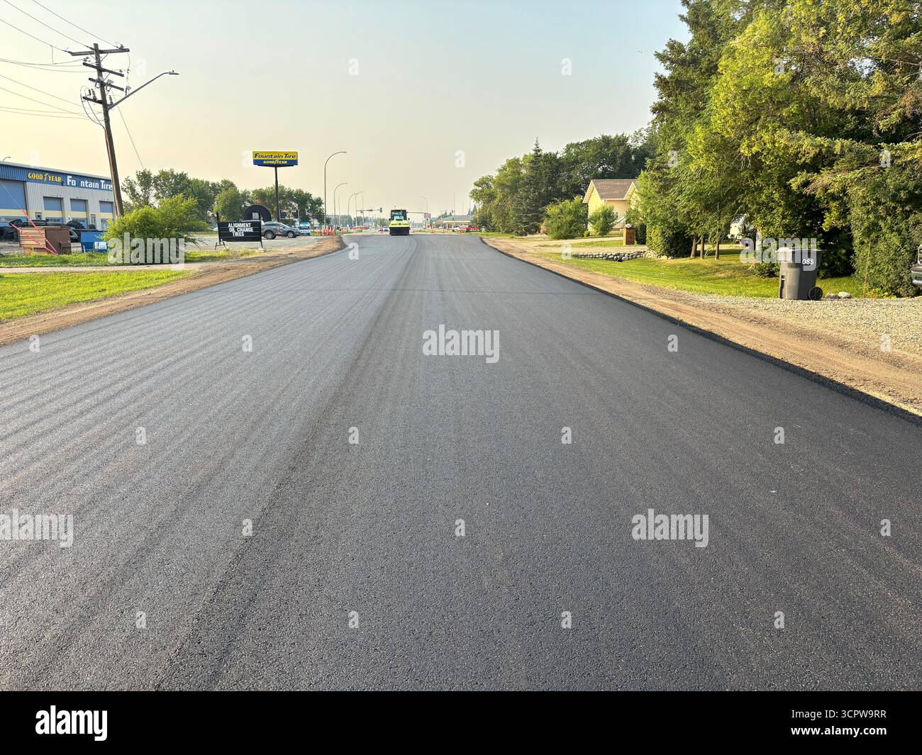 Freshly paved residential street, showing smooth new asphalt surface, roadside trees, and power lines in a suburban neighbourhood. - Smartphone Captured Stock Image
