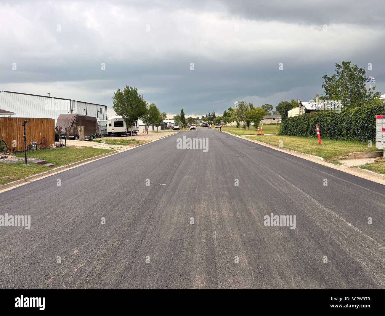 Freshly paved residential street, showing smooth new asphalt surface, and roadside trees in a suburban neighbourhood. - Smartphone Captured Stock Image