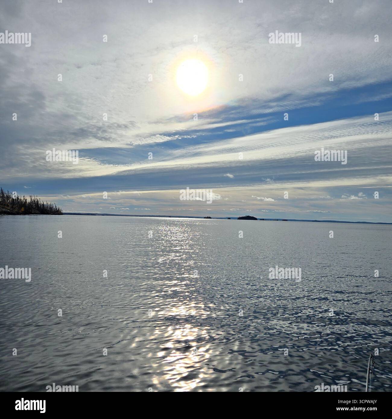 Sunlit Northern lake with rippling waters and a forested shoreline under partly cloudy sky at midday. - Smartphone Captured Stock Image