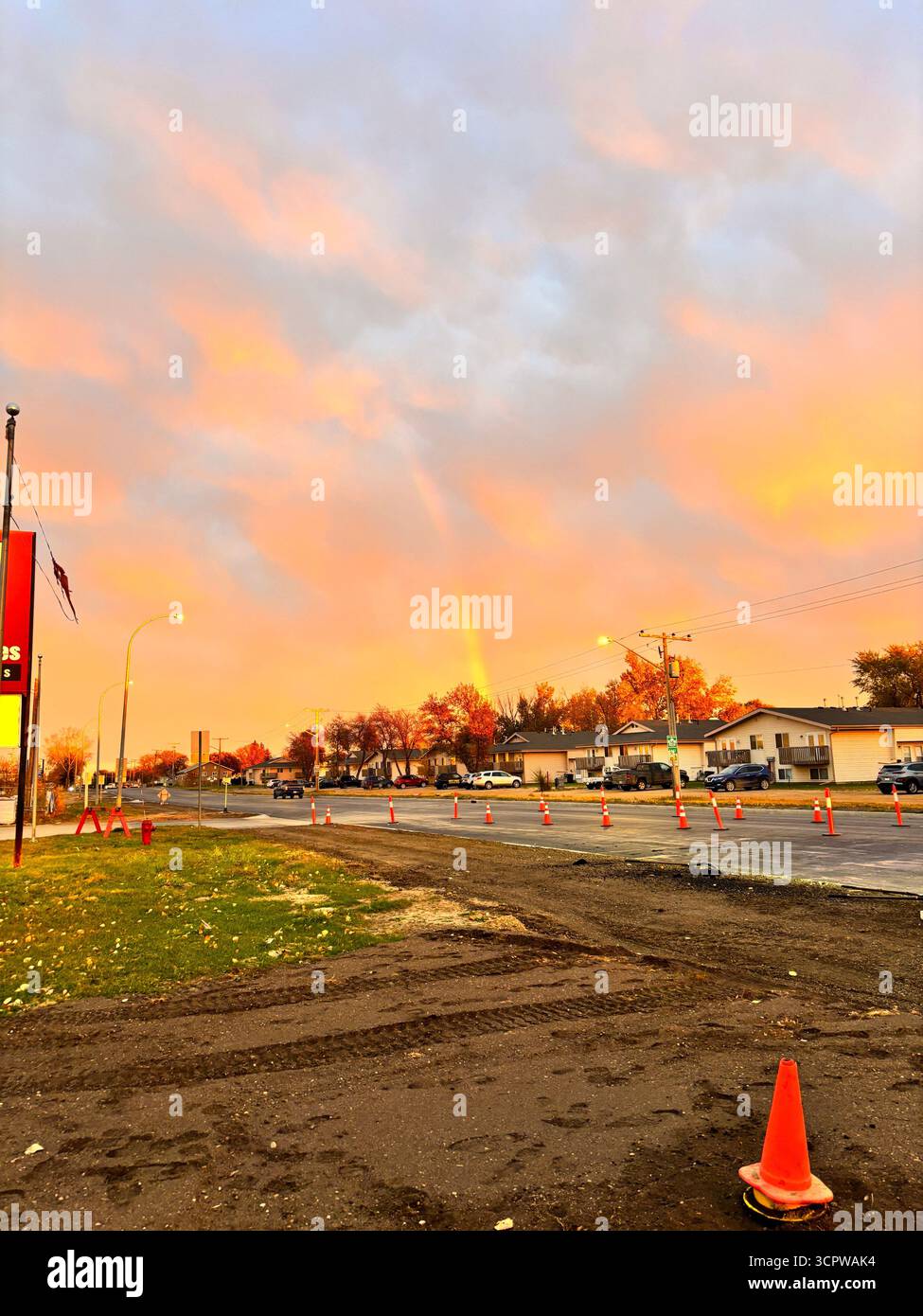 Rainbow over a road construction site at sunset, with orange cones and houses under a colourful sky. - Smartphone Captured Stock Image