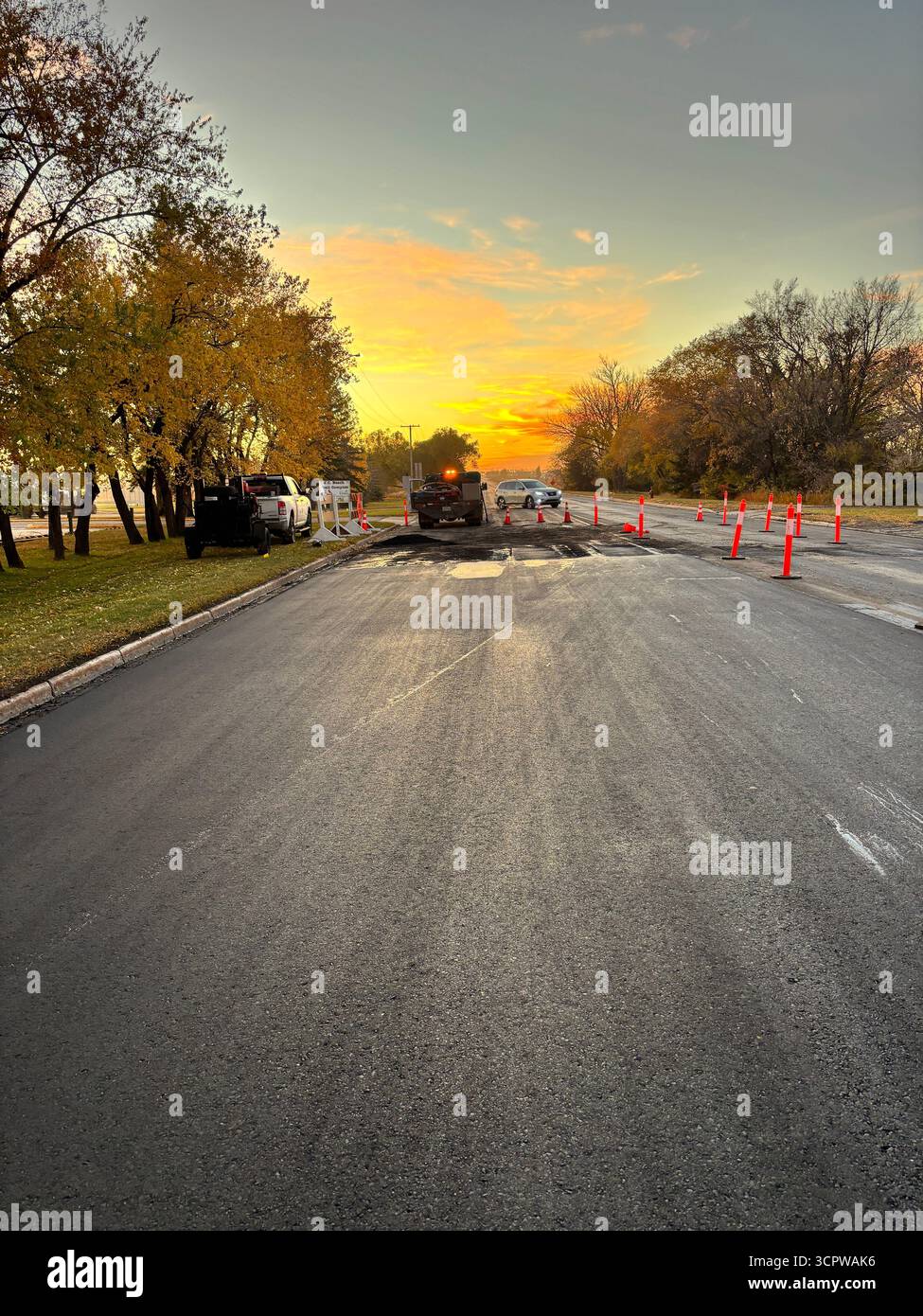 Road construction at sunrise with orange cones, trucks, and autumn trees under a vibrant orange sky. - Smartphone Captured Stock Image
