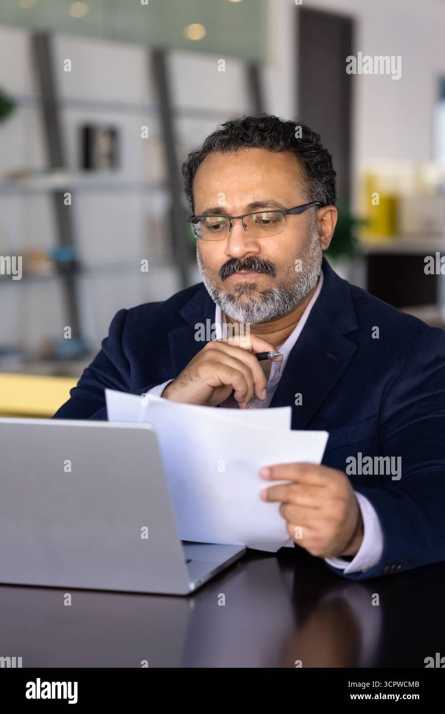 Focused businessman carefully reading printed documents while sitting at desk Stock Photo