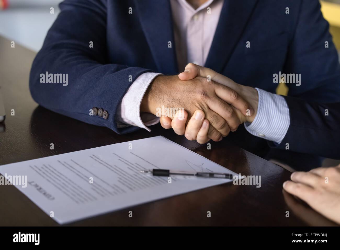 Two business professionals firmly shaking hands over signed contract Stock Photo