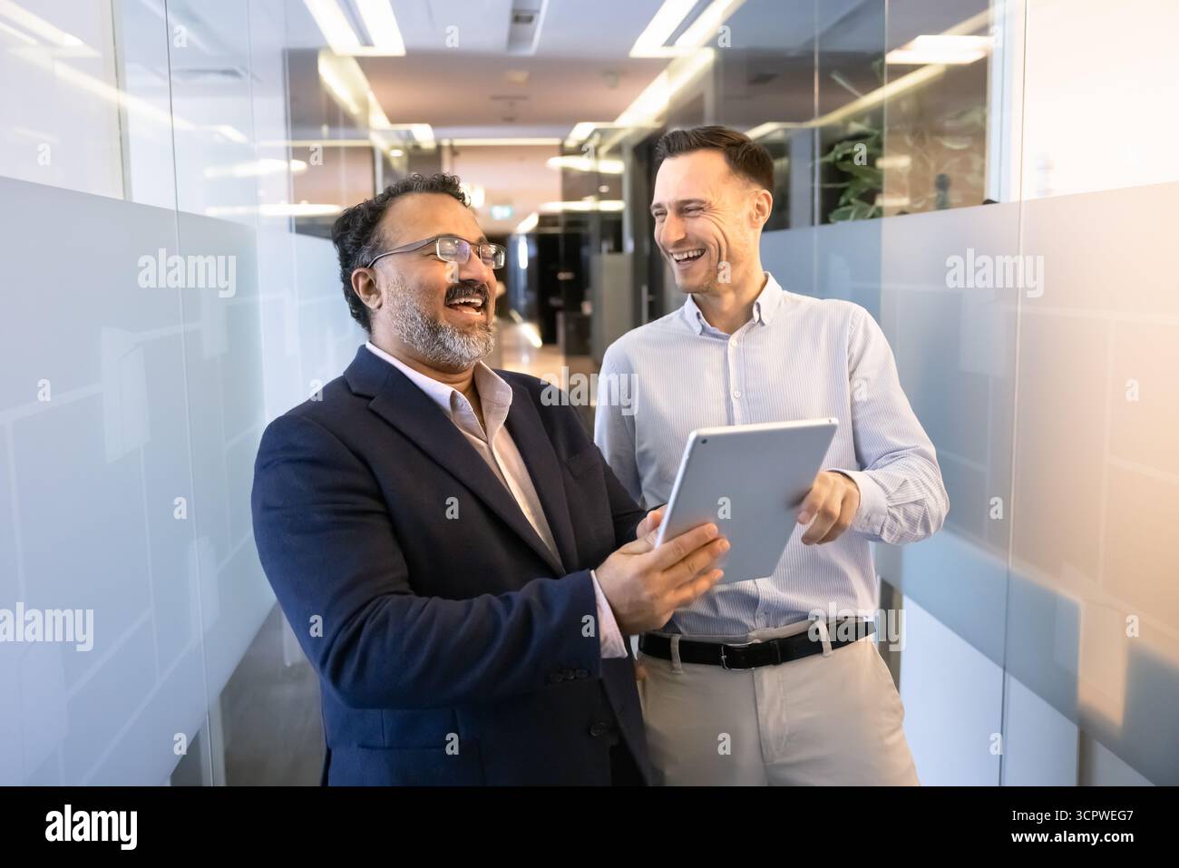 Two businessmen laughing, discussing work-related matters or content on tablet Stock Photo