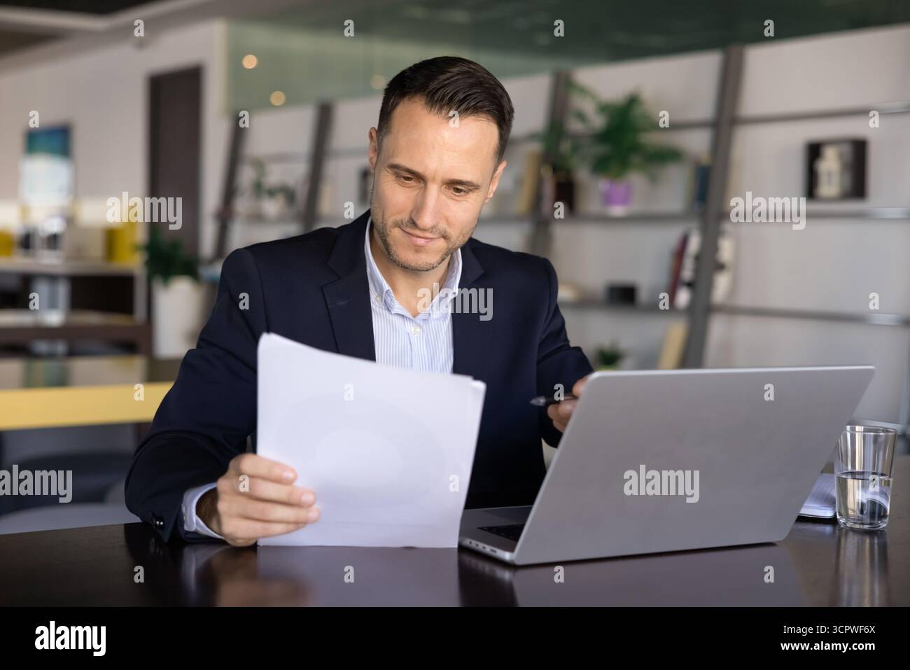Businessman reviewing printed documents while working on laptop Stock Photo