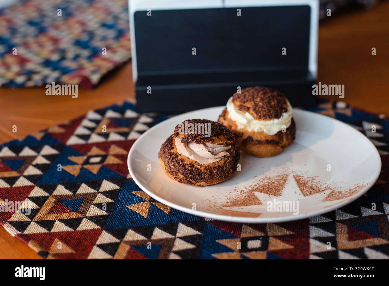 Two cream puffs on a white plate with a geometric-patterned tablecloth. Stock Photo