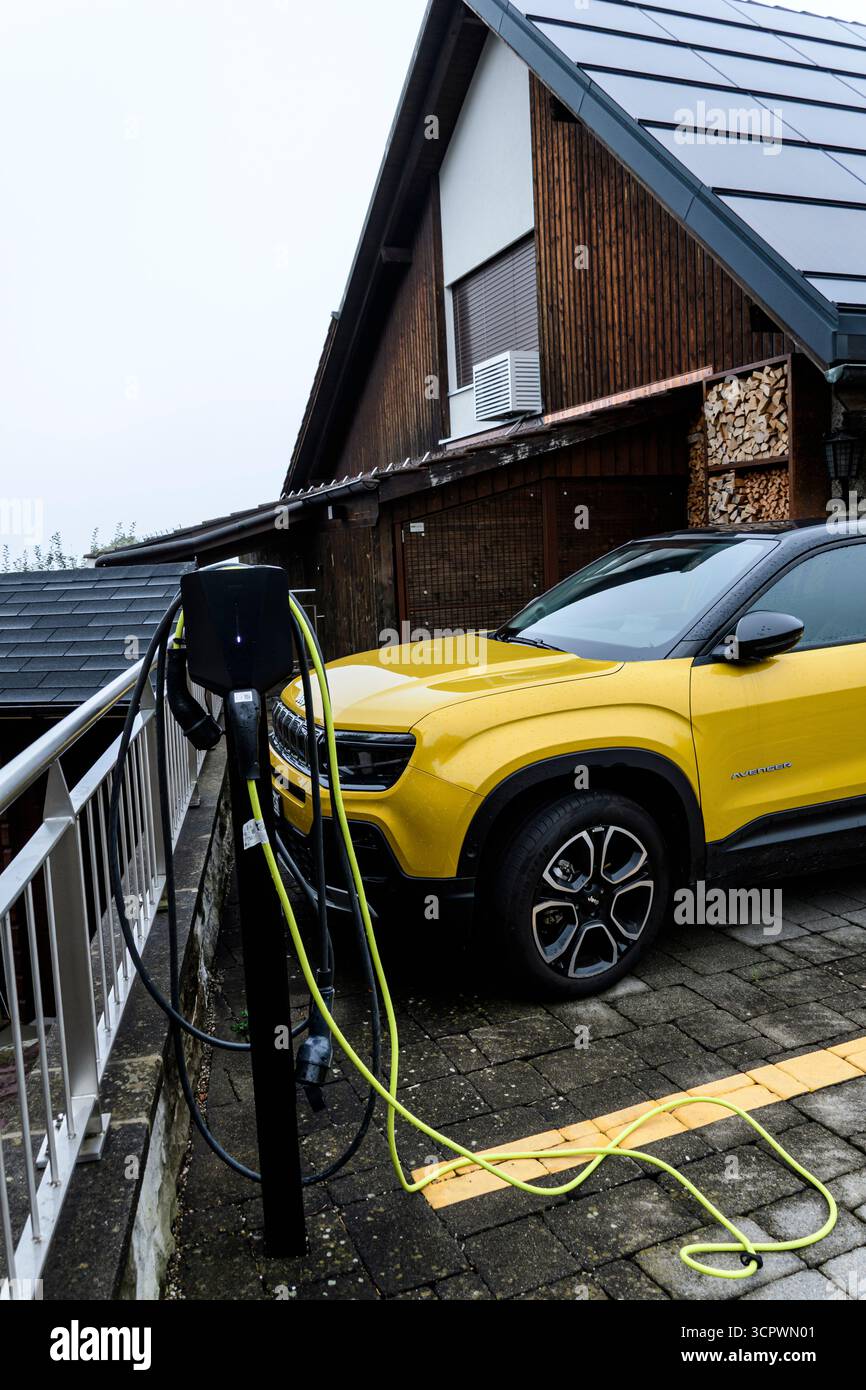 Electric car parked near a battery charger besides a luxury wooden house, Höhenstrasse, Hinwil, Zurich, Switzerland Stock Photo