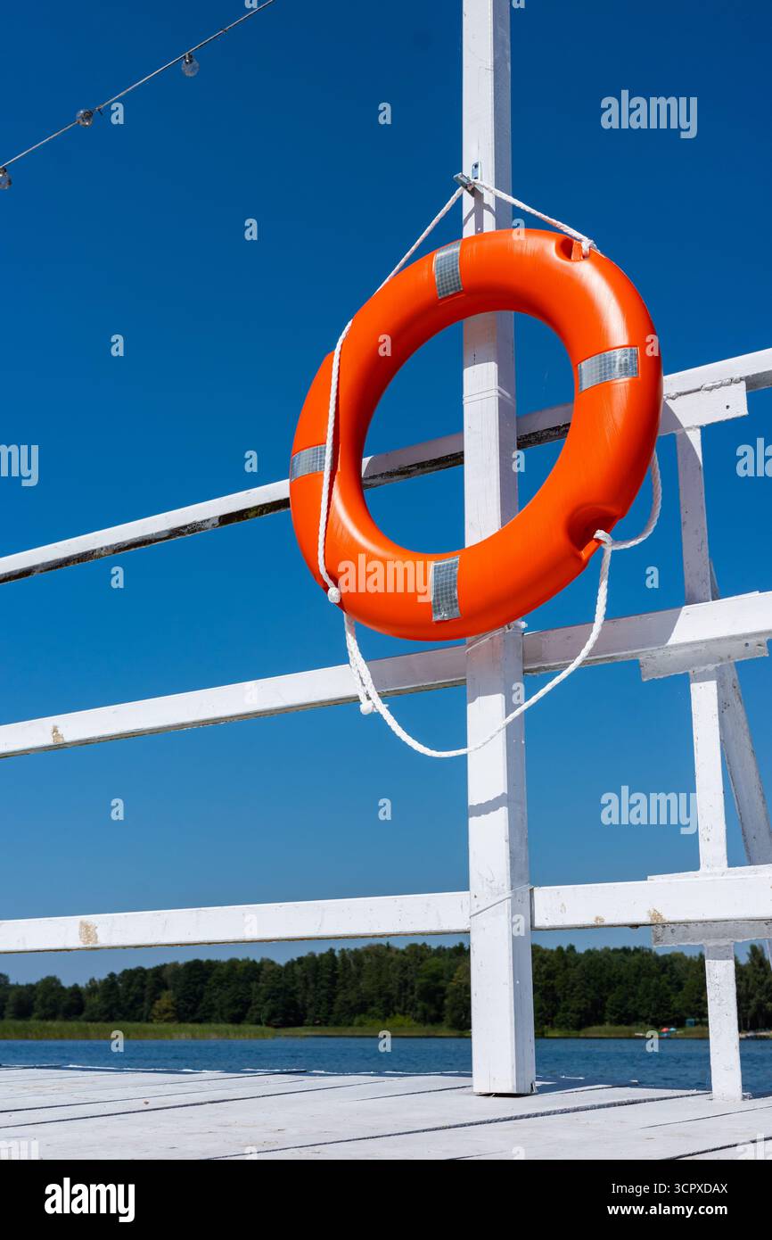 Orange swimming rescue wheel hanged on the rails of the white jetty ...