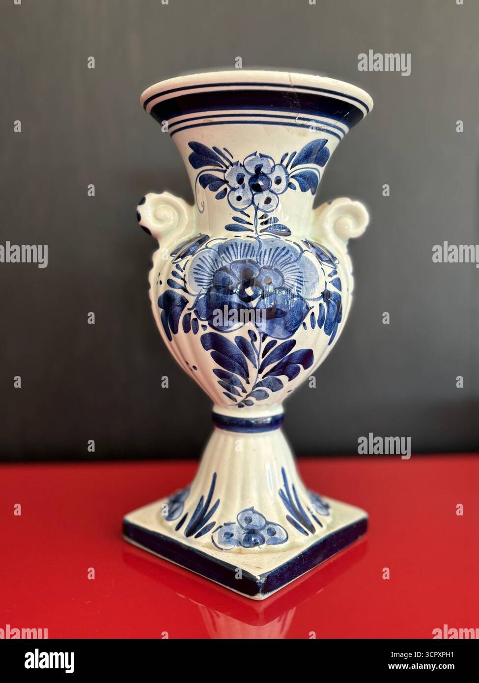 A medium-sized Delftware vase on a red cabinet (surface) and in front of a black wall. - Smartphone Captured Stock Image
