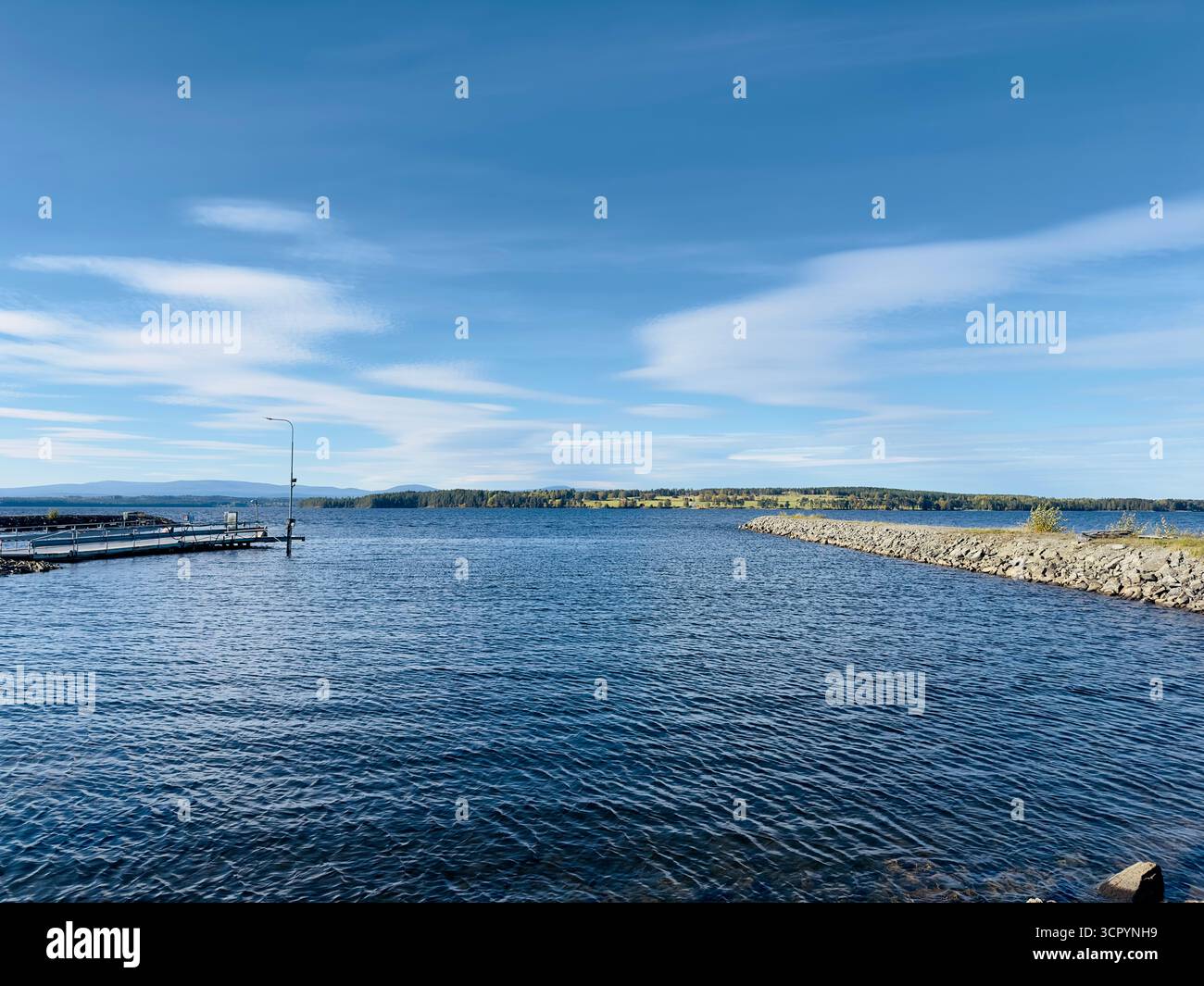 Serene view of the lake under a bright blue sky with wispy clouds. - Smartphone Captured Stock Image