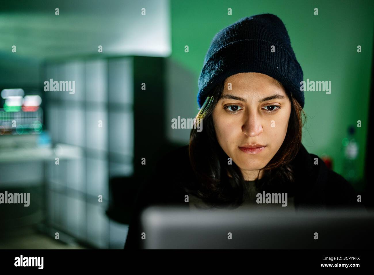 Female young hacker working on computer in dark room programming code Stock Photo