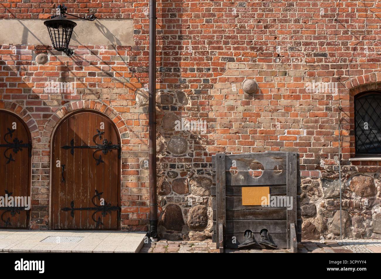 Fragment of inner castle courtyard. Vintage medieval whipping post, pillory, wooden framework with holes for securing head and limbs. Świdwin, Poland. Stock Photo