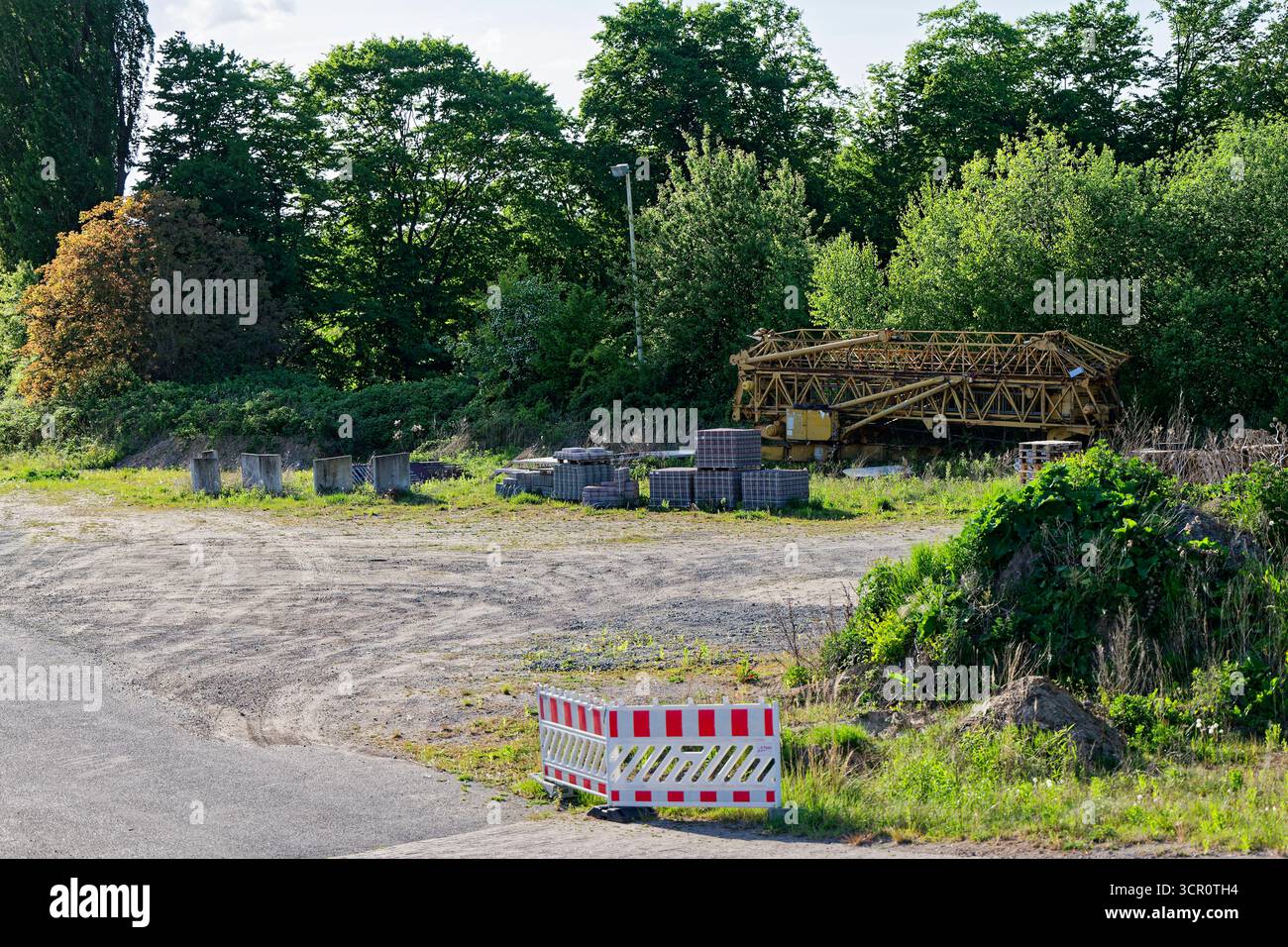 A small road exit is blocked by two safety barriers. A mobile crane ...