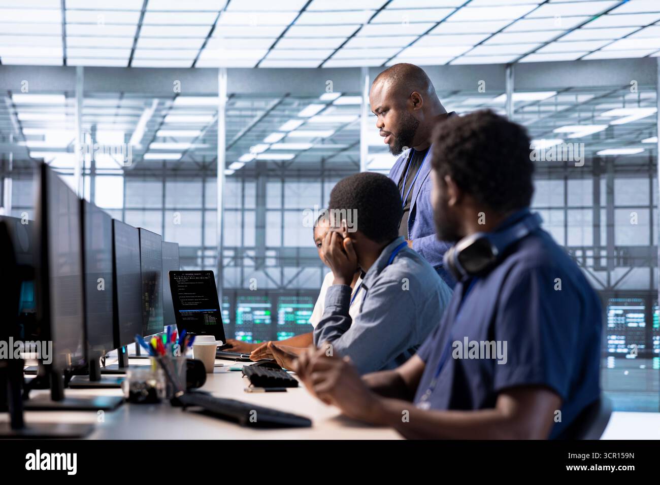 Team of data center office system administrators using programming languages to construct algorithms and build applications. African american server farm IT professionals debugging and optimizing code Stock Photo