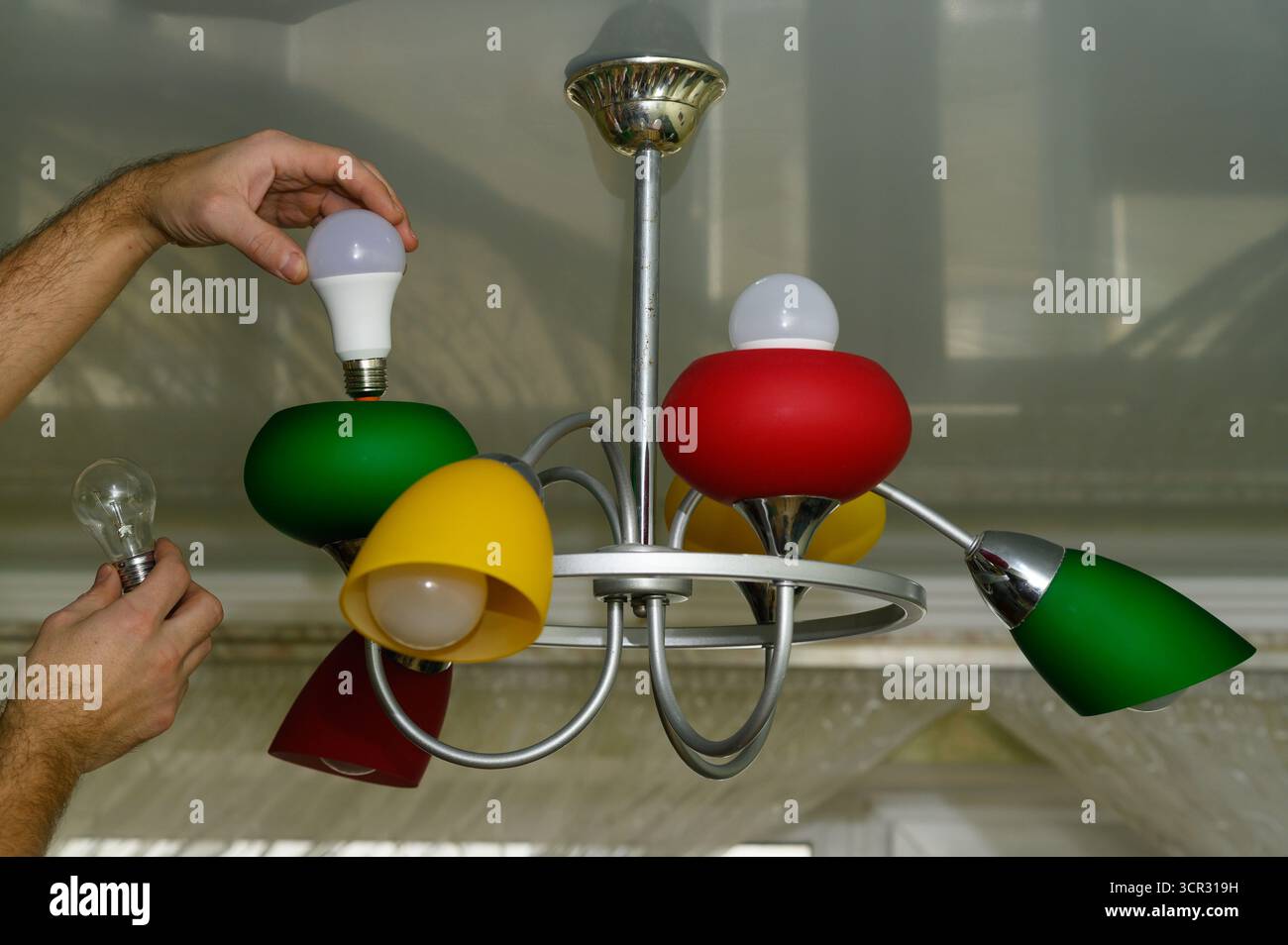 Man prepares to switch lamp by replacing incandescent bulb with LED version. Lamp becomes symbol of environmental responsibility and smart power use. Stock Photo