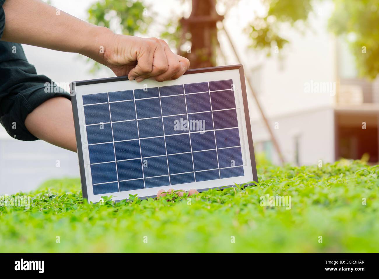 Young man hands standing in the park and holding photovoltaic mini solar panel over the bush. Concept of renewable energy, technology. Stock Photo
