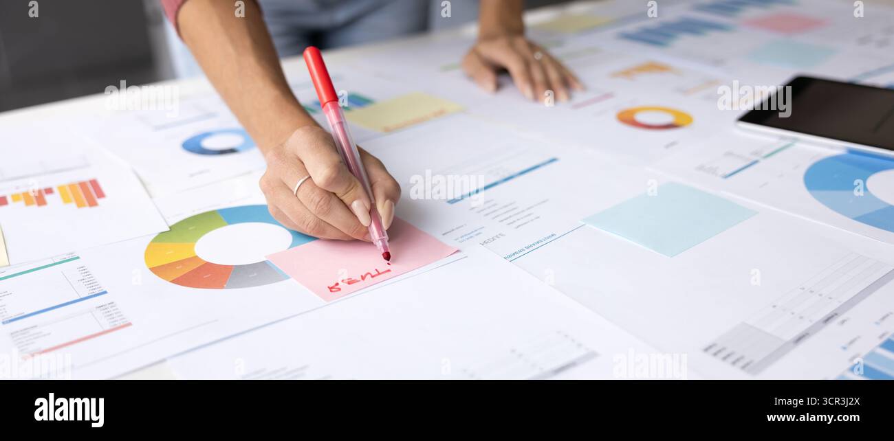 Female writes on sticky note, working in office at table Stock Photo