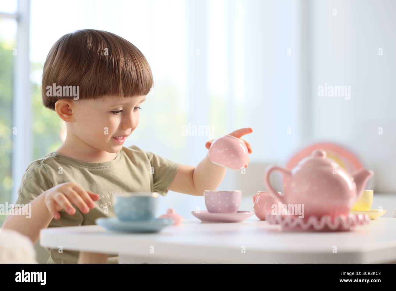 Cute little boy playing with toy tea set at table indoors. Space for ...