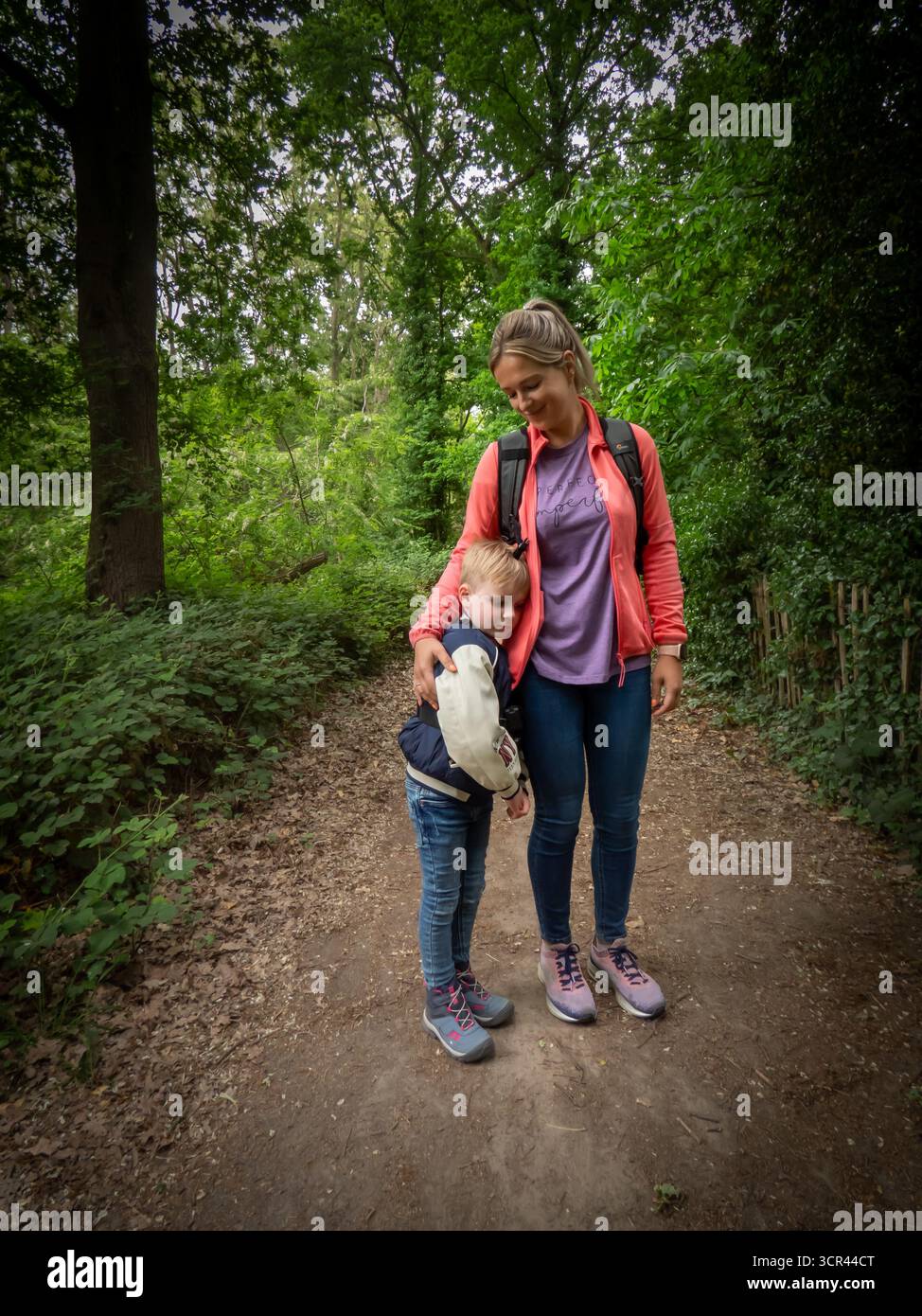 Mother and child walking on forest trail surrounded by green trees Stock Photo