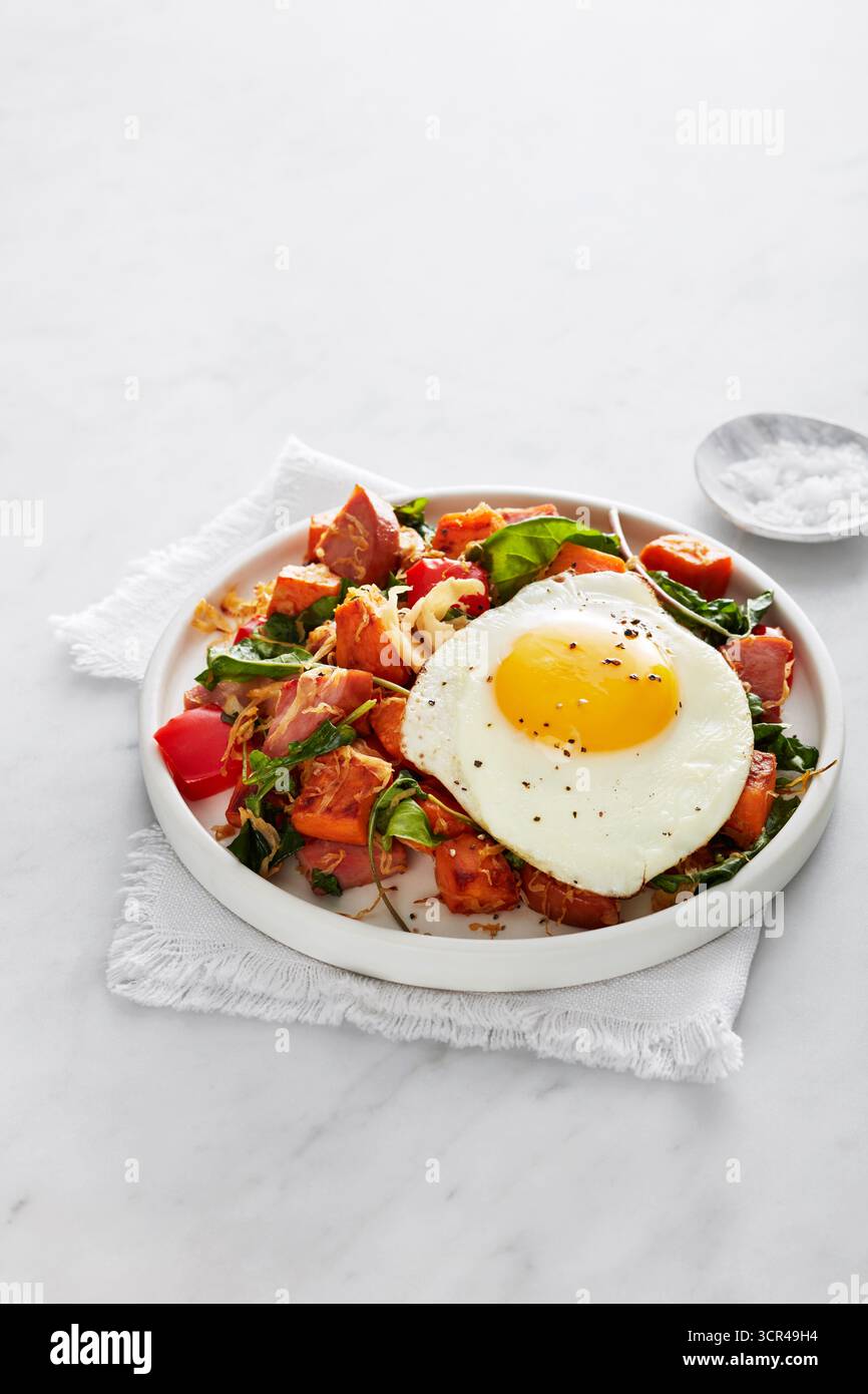 A plate of hash with sweet potatoes, greens, and a sunny-side up egg on ...