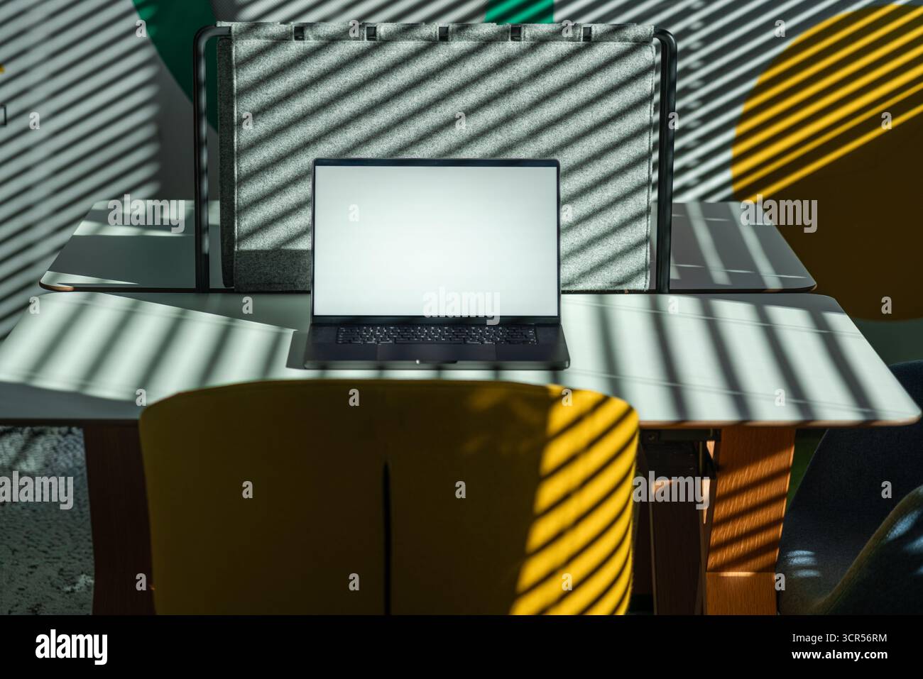 Laptop Workspace Shadows Light Interior office space Creative modern office scene with open laptop on shared desk, dramatic sunlight filtering through Stock Photo