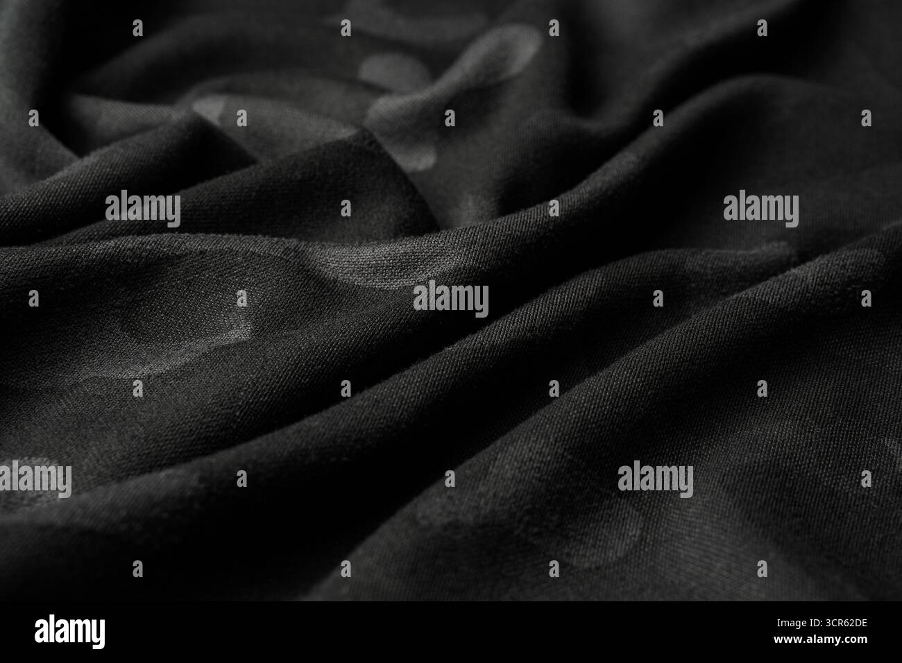 Black, draped fabric with subtle camouflage spots and shallow depth of ...