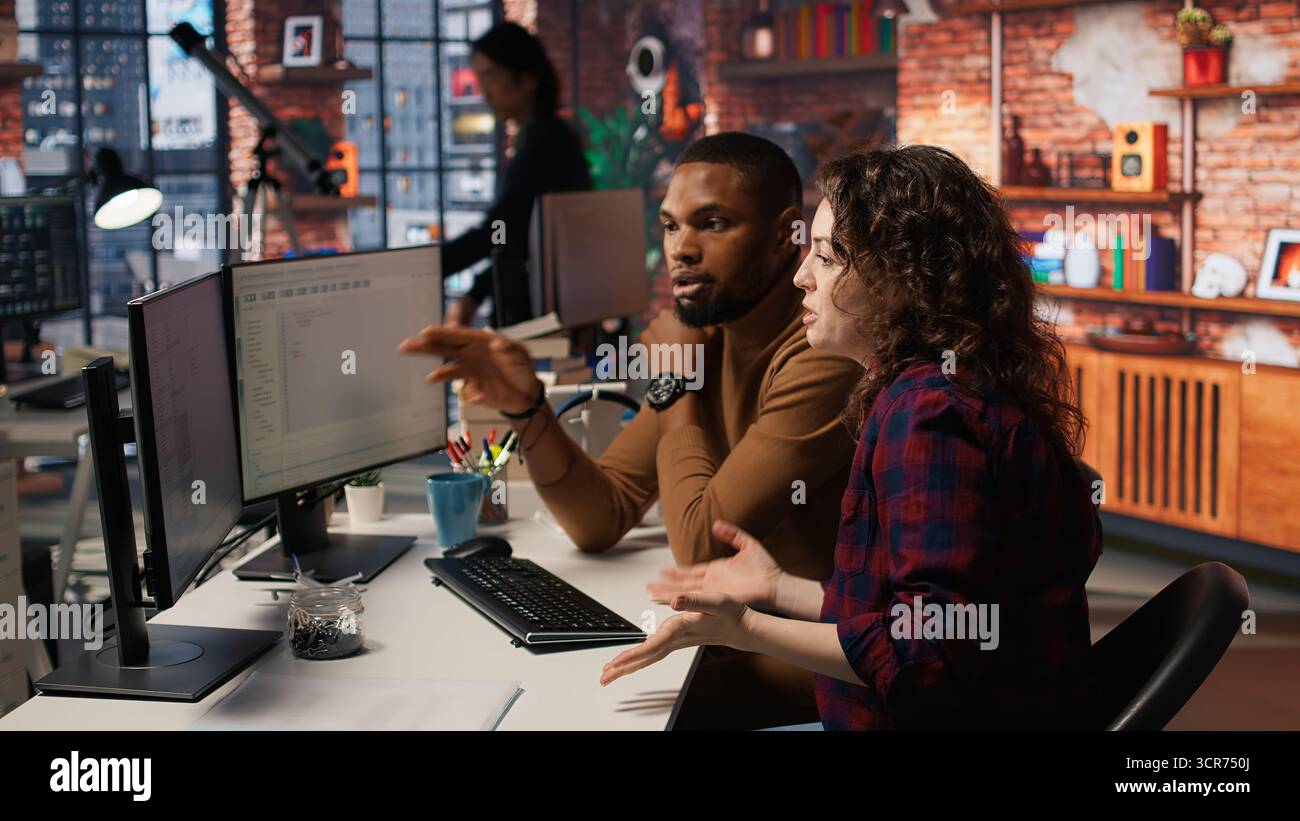 Engineers cooperating in startup office, using programming languages on PC to build applications. Coworkers doing brainstorming, using computer in software development agency to code, camera A Stock Photo