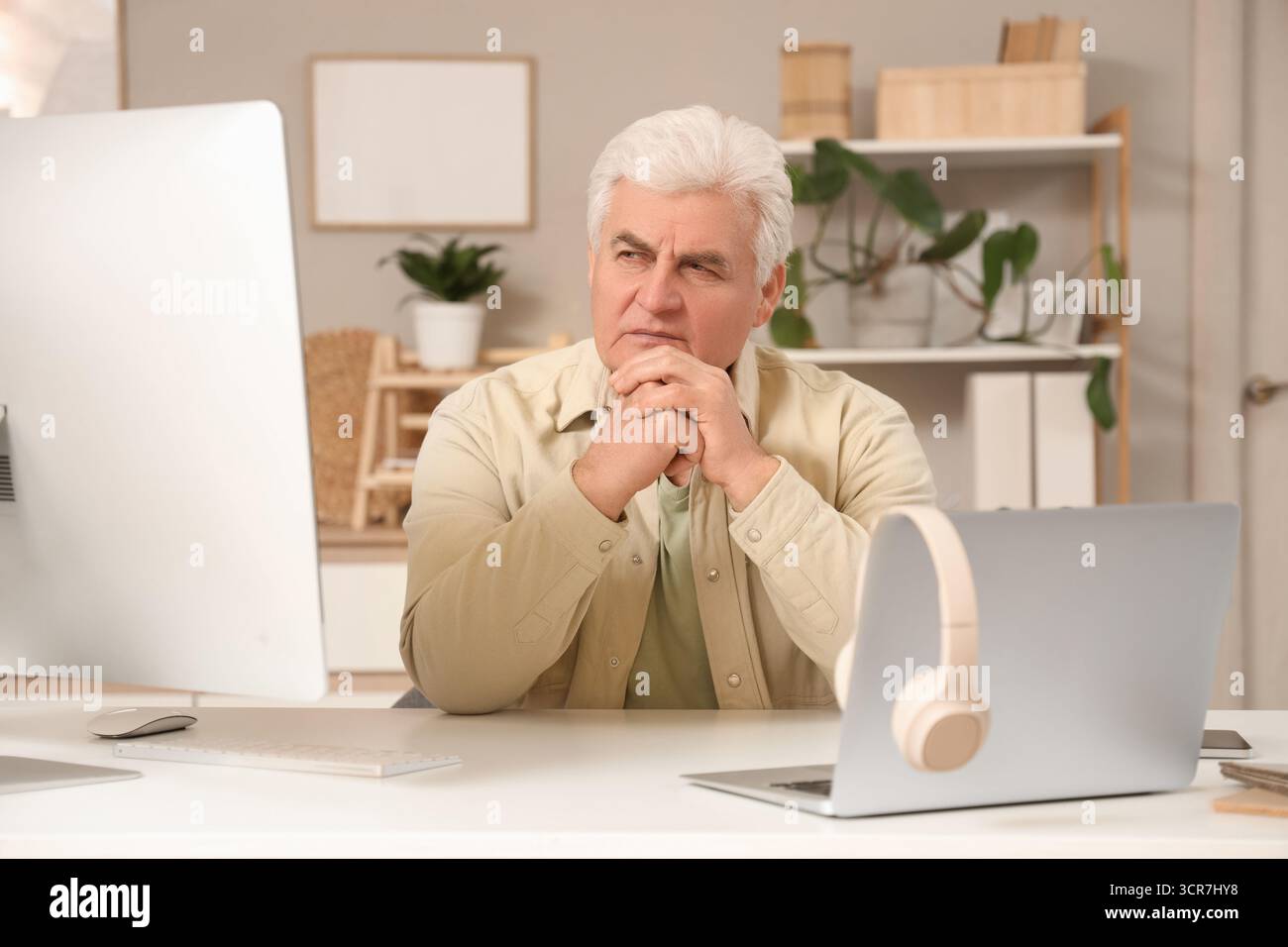 Thoughtful senior programmer working at desk in office Stock Photo
