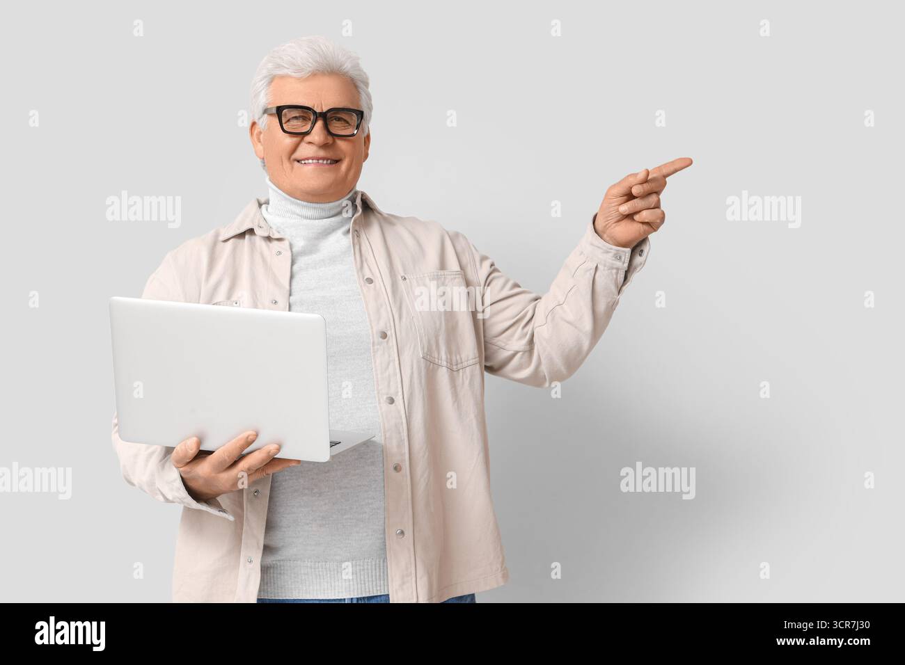 Senior programmer with laptop pointing at something on light background Stock Photo