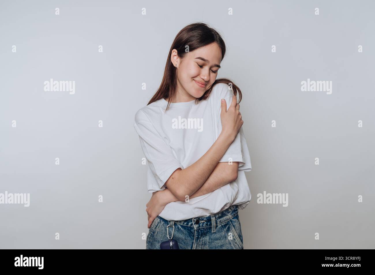 Woman embracing herself with a warm smile in a simple indoor setting Stock Photo