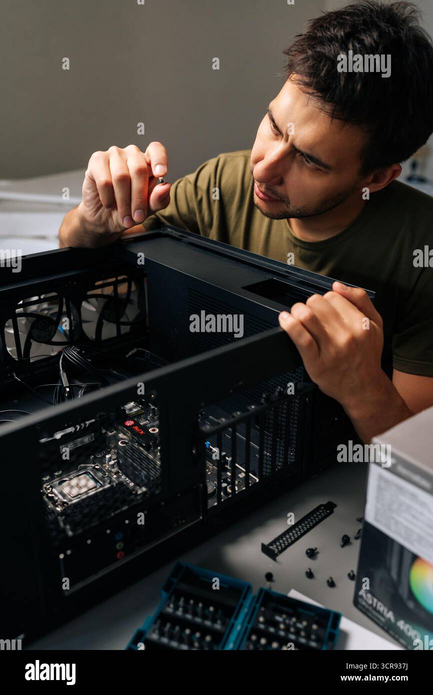 Vertical portrait of computer technician installing internal hardware components, precision-focused working inside desktop pc case, optimizing system Stock Photo