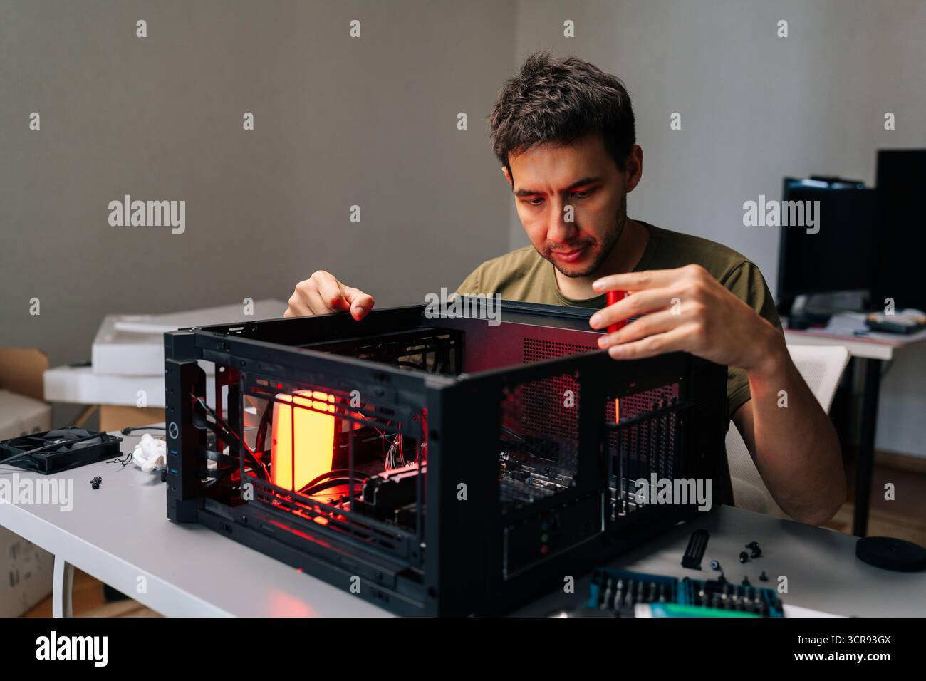 Computer technician installing components inside desktop computer case, illuminated by red light, performing maintenance or upgrade. Stock Photo