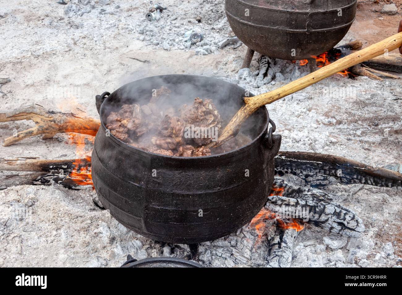 african village boiling beef meat in a cauldron three legged pot ...