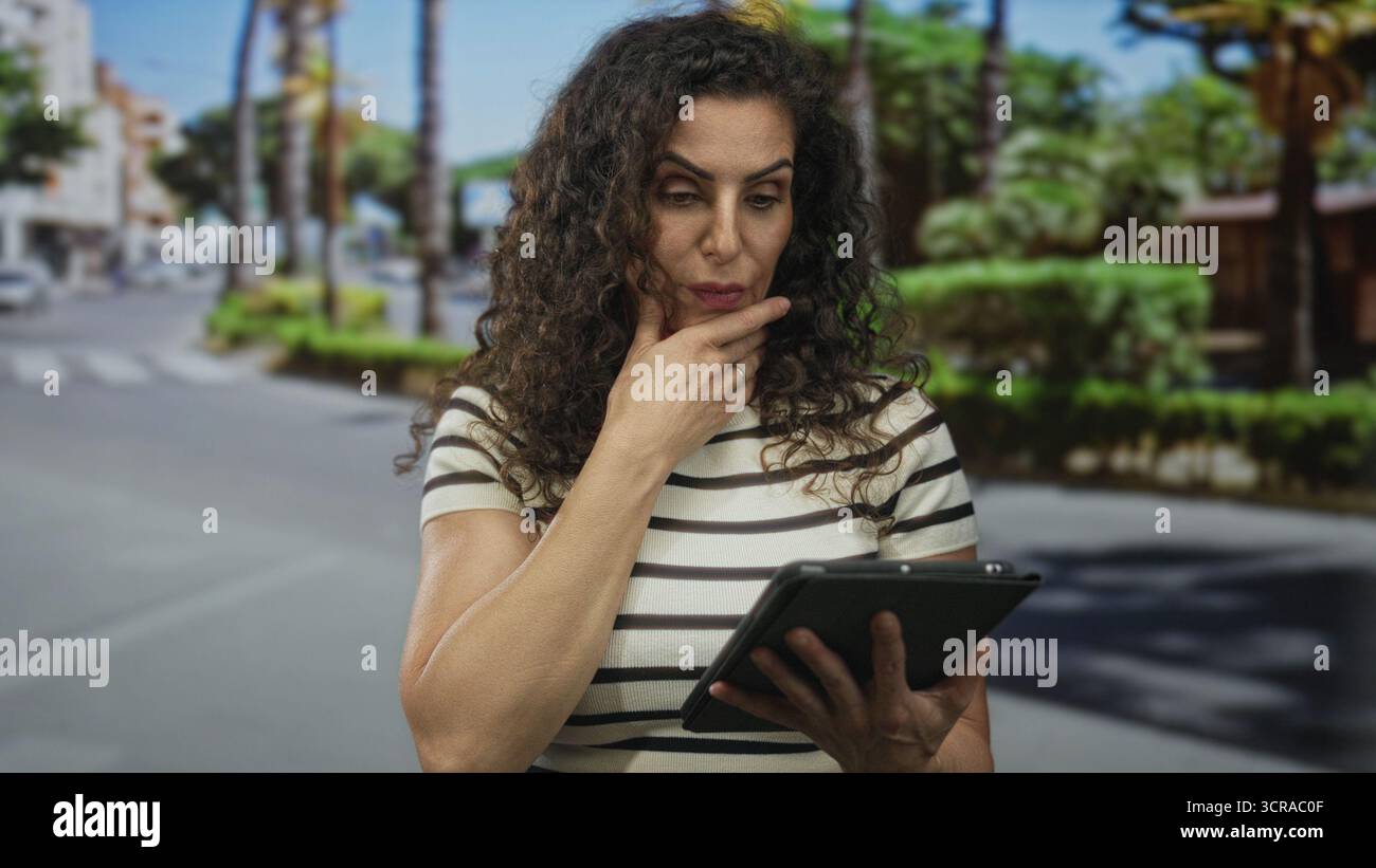 Woman on city street holding tablet with one hand and touching forehead with the other while staring at screen; surprise. Stock Photo