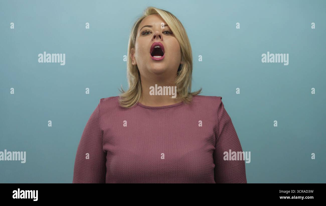 Blonde woman pinches nose wearing a mauve top in a light blue studio set reacting to a foul smell; disgust. Stock Photo
