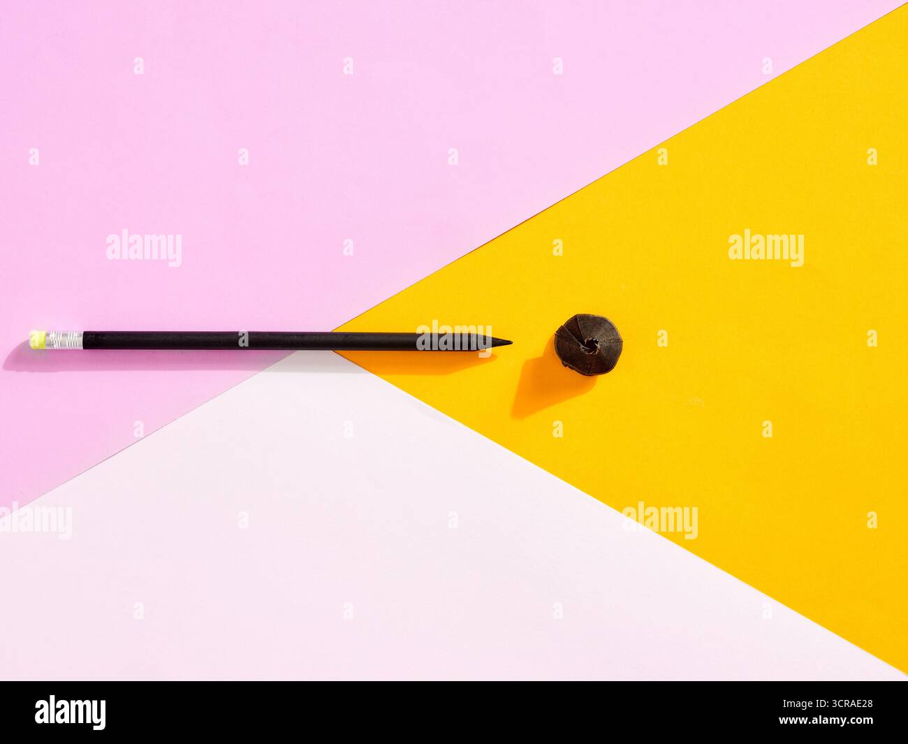 Black pencil and shavings arranged on a vibrant pink, white, and yellow geometric background, forming a contemporary art composition Stock Photo