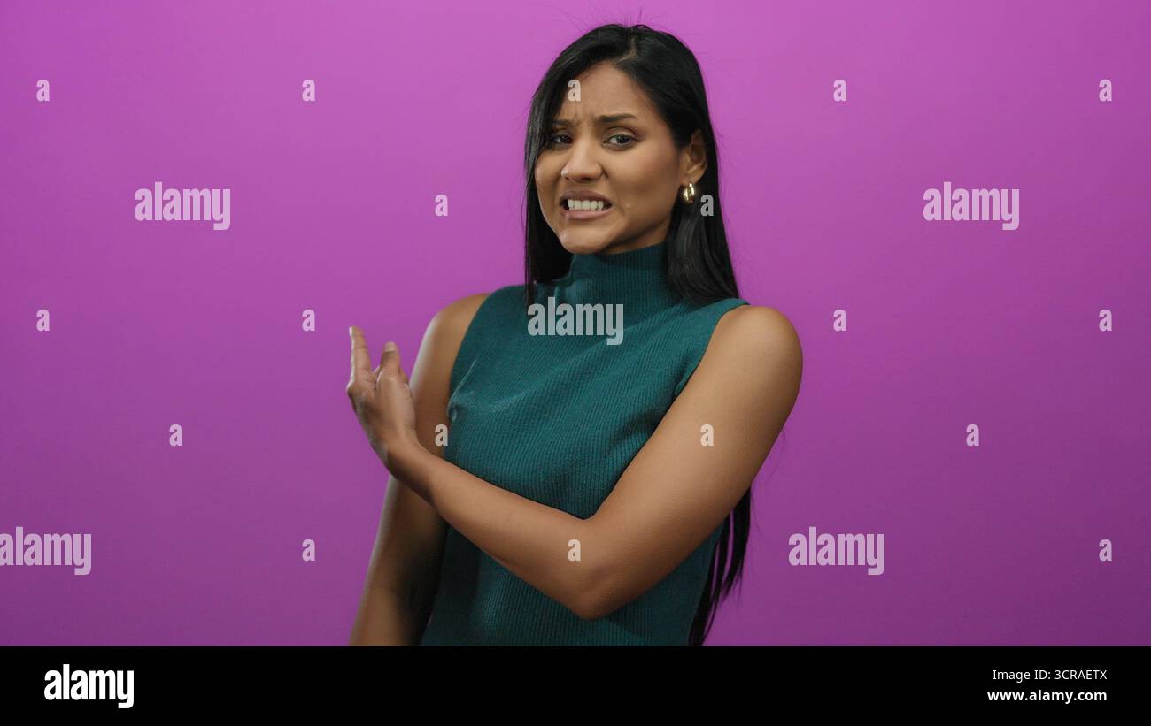 Woman expressing uncertainty against a vivid pink background, pointing with both hands, dressed in teal, displaying mixed emotions, isolated for conce Stock Photo