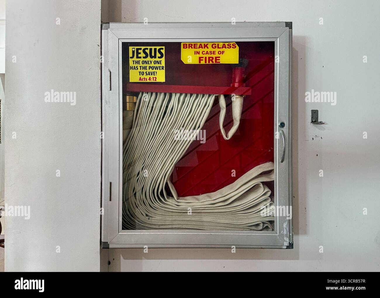 Contrasting juxtaposition, Philippines: fire hose cabinet, religious sticker JESUS THE ONLY ONE HAS POWER TO SAVE! (Acts 4:12) beside BREAK GLASS sign - Smartphone Captured Stock Image