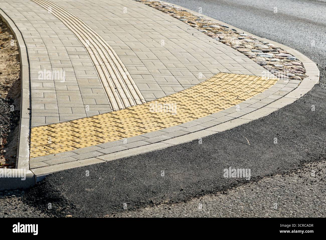 Urban sidewalk with tactile paving and guidance strips for accessibility at pedestrian crossing Stock Photo