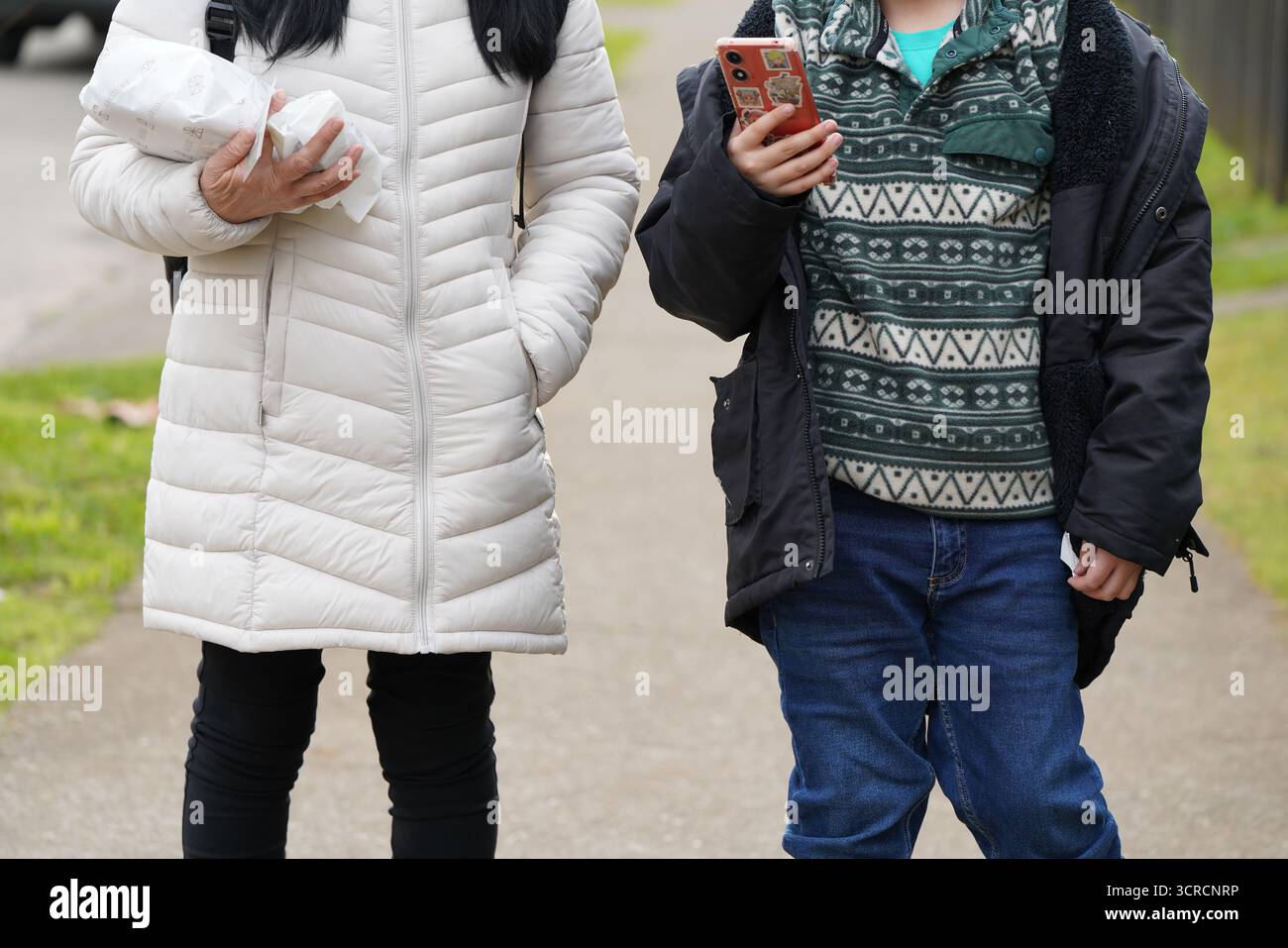 niño mirando su celular junto su madre Stock Photo