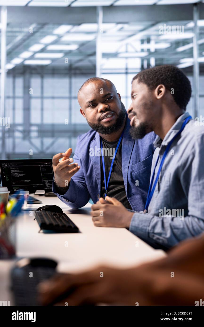 Data center admin discussing with coworker, using programming languages to construct algorithms and build applications. Server hub IT specialist talking with colleague, debugging and optimizing code Stock Photo